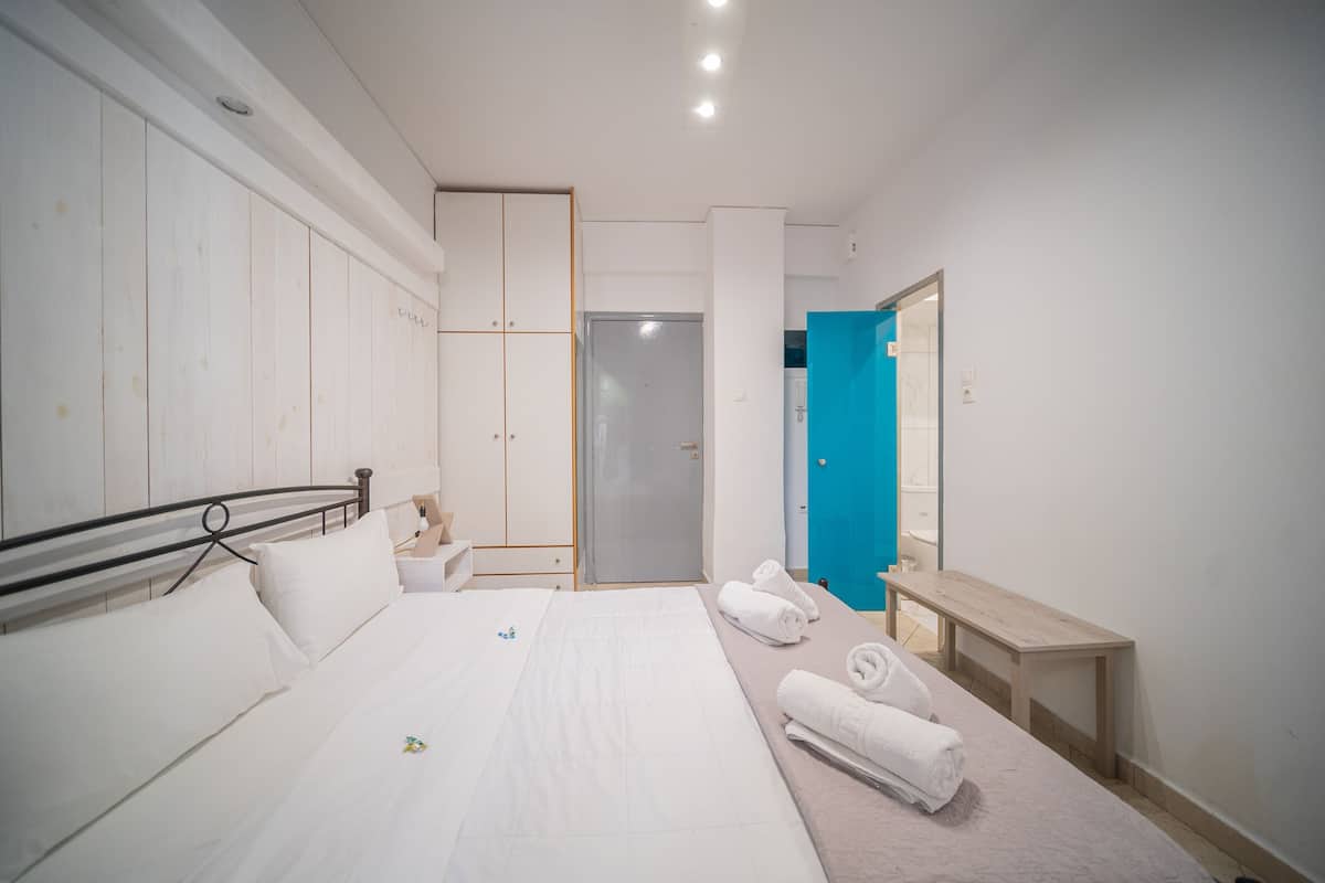 A modern hotel room with a large bed, a bedside table, a bench, and a wardrobe.
