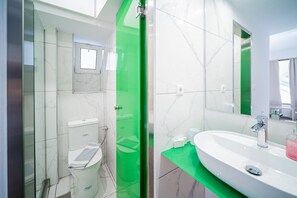 Uma casa de banho moderna com sanita branca, cabine de duche verde, lavatório branco com espelho e parede com mosaicos de mármore.
