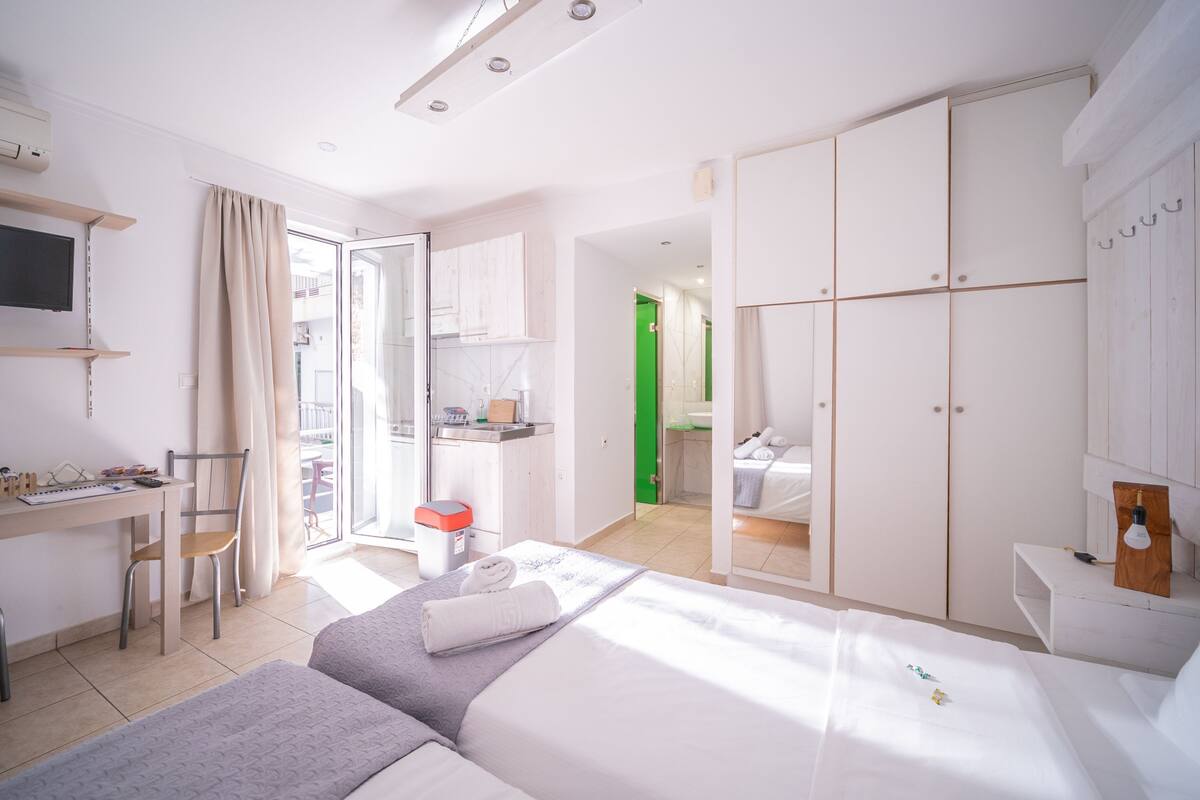 A modern hotel room with a bed, desk, chair, wardrobe, and a view of the outside.