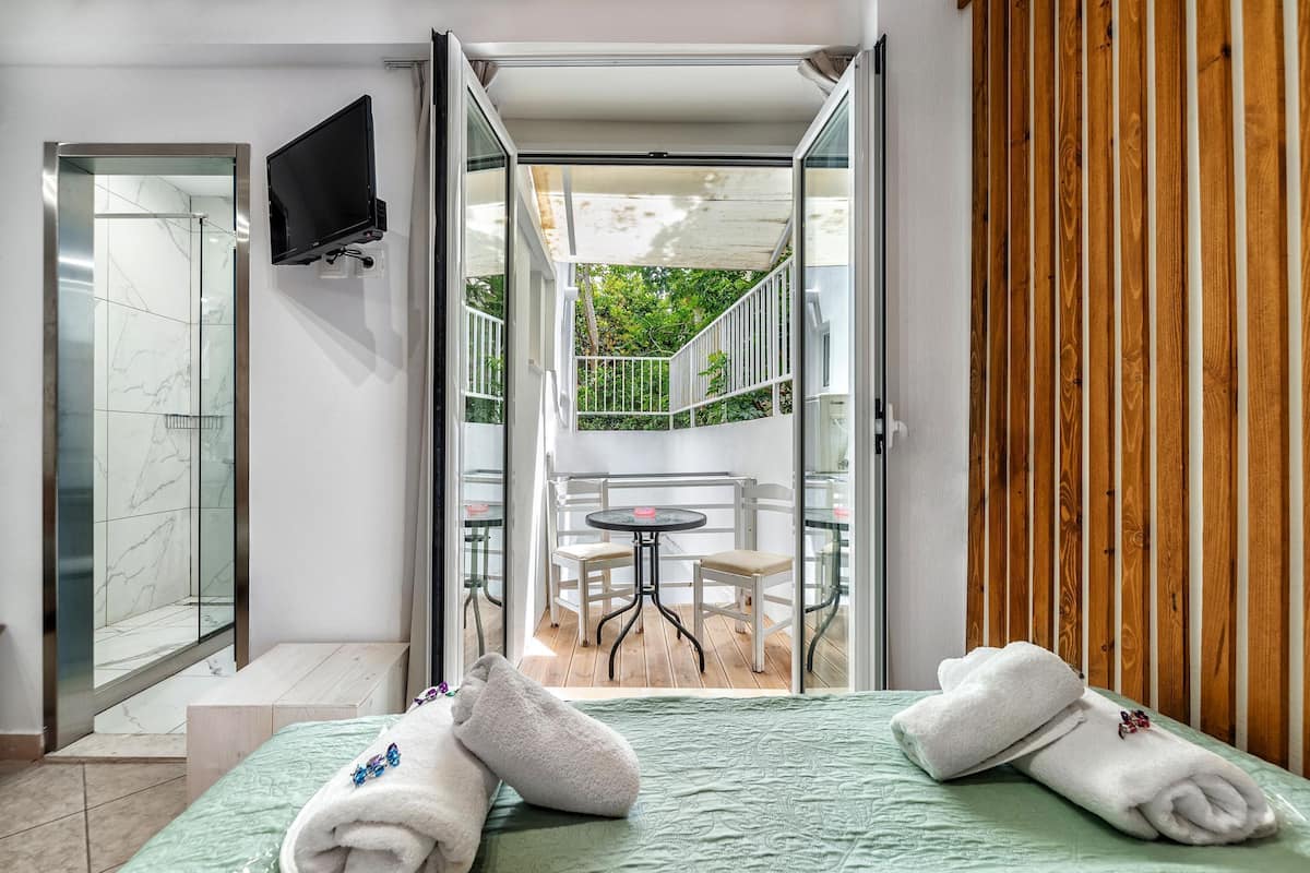 A hotel room with a bed, a bench, a TV, and a balcony with a table and chairs.