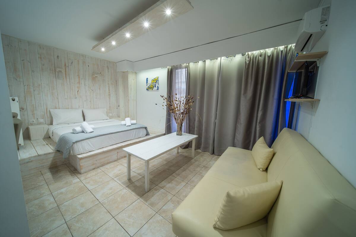 A modern hotel room with a bed, a sofa, a coffee table, and a TV on a shelf.