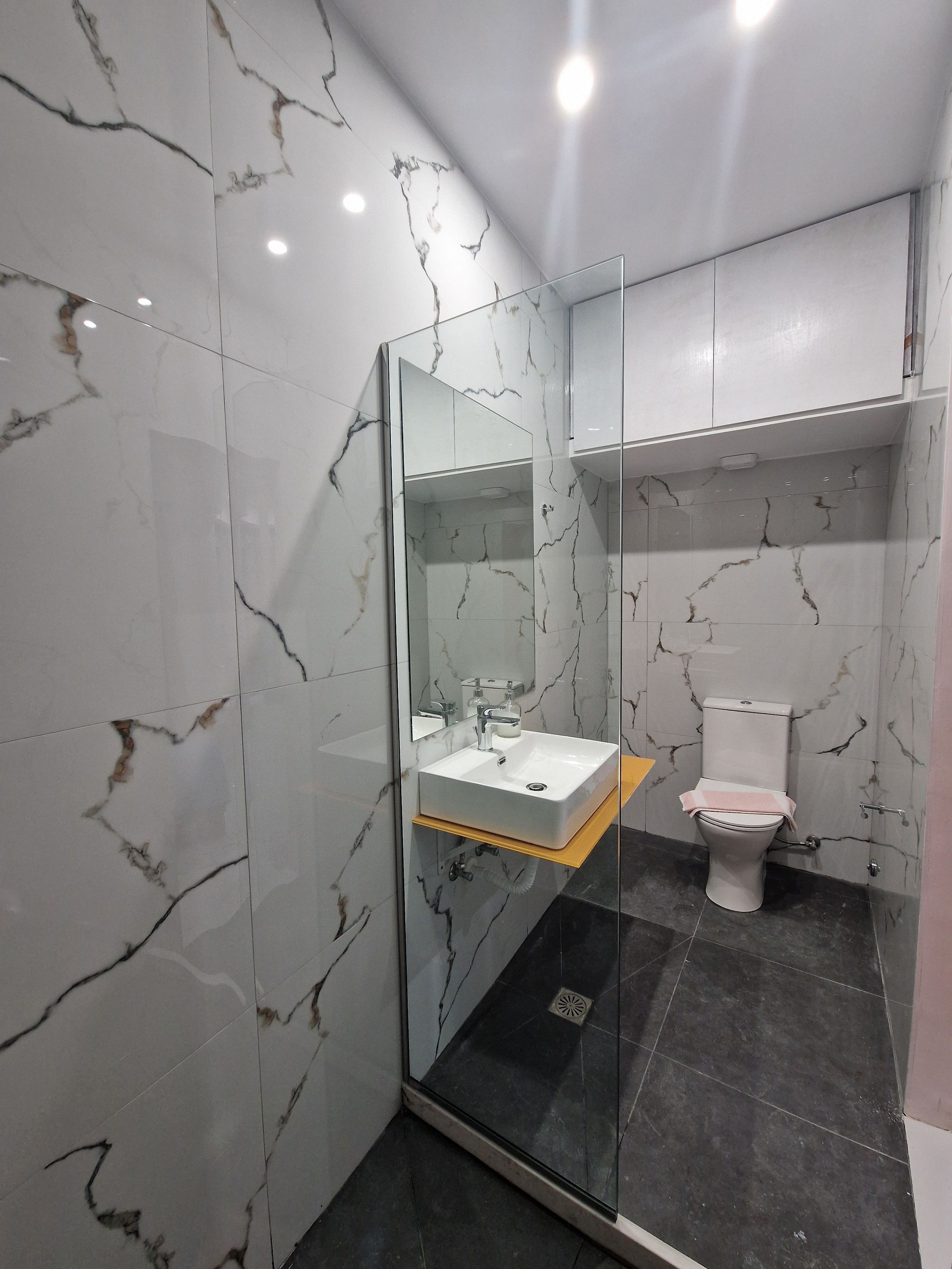 A modern bathroom with a glass-enclosed shower, a white sink, and a toilet.