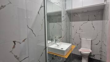 A modern bathroom with a glass-enclosed shower, a white sink, and a toilet.
