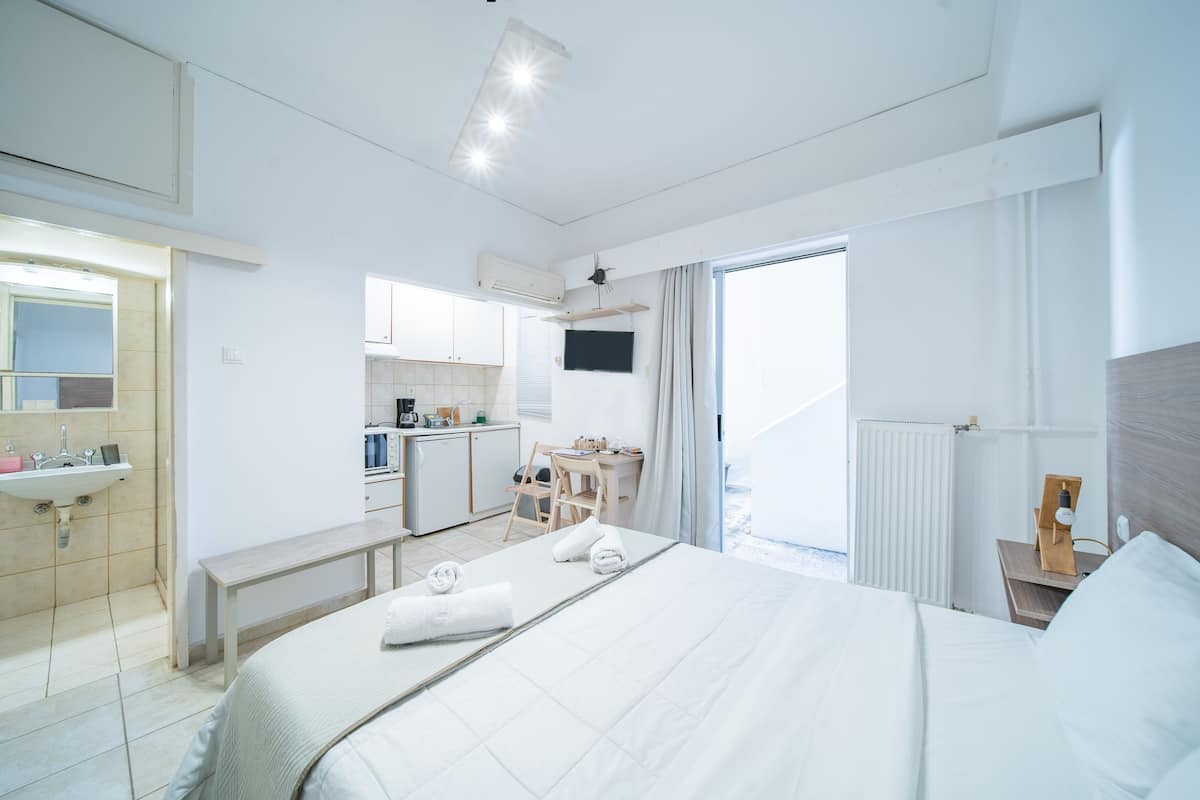 A hotel room with a bed, a desk, a chair, a small kitchenette, and a bathroom.