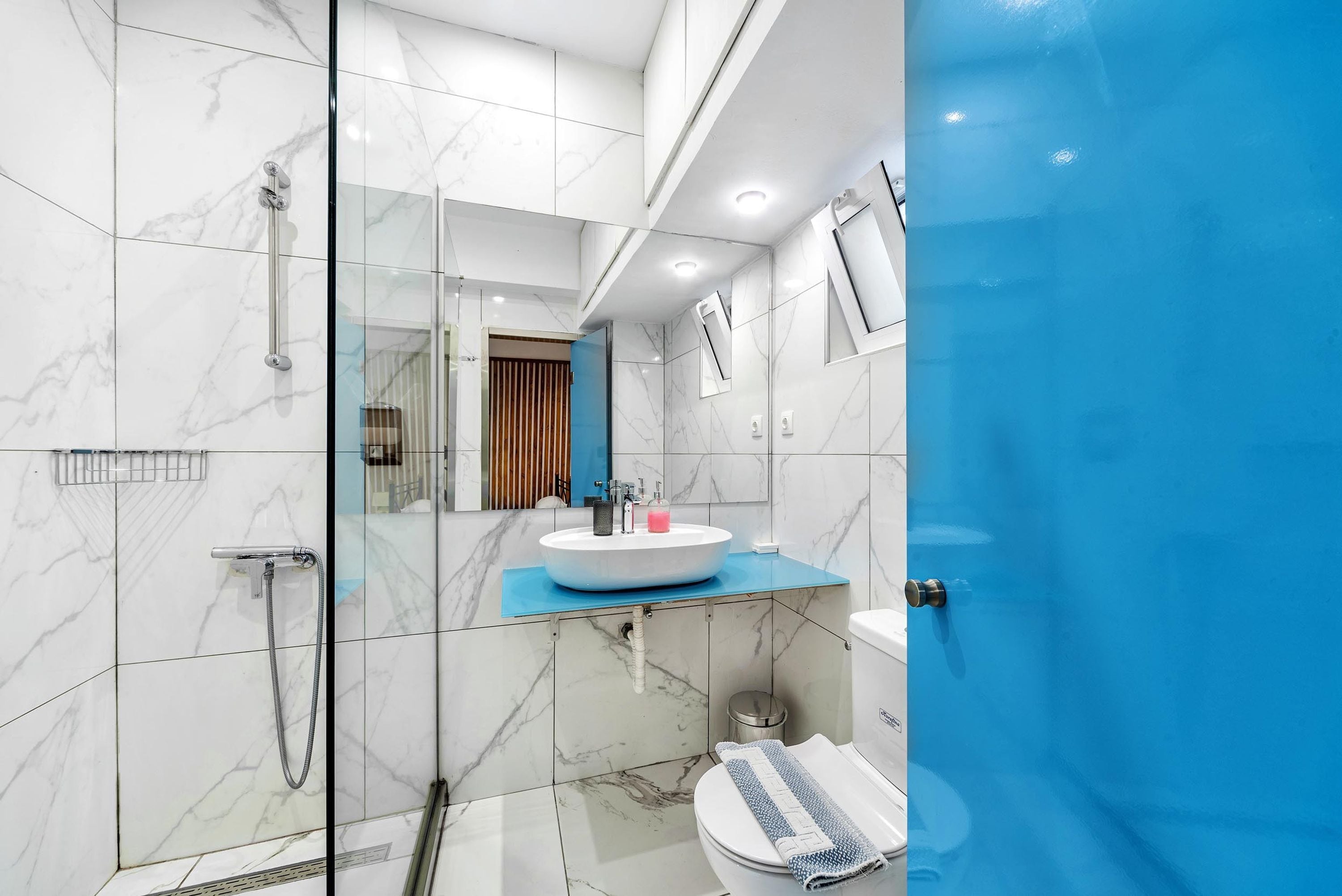 A modern bathroom with a glass-enclosed shower, a white sink with a blue countertop, and a toilet with a towel.