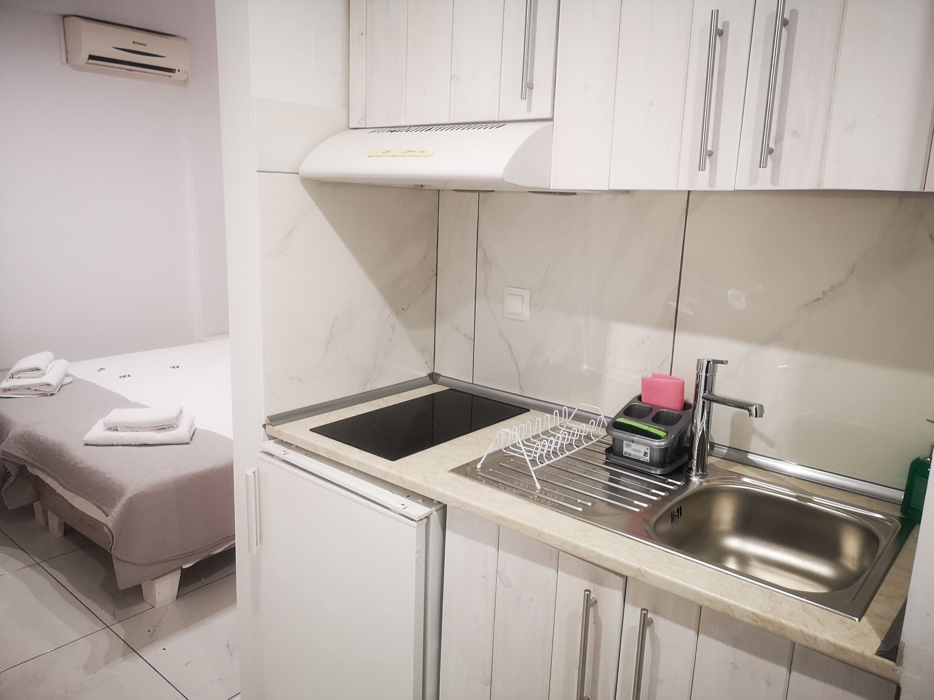 A compact kitchenette with a sink, stove, and a small countertop. There is a towel rack with folded towels and a small table with a bench.