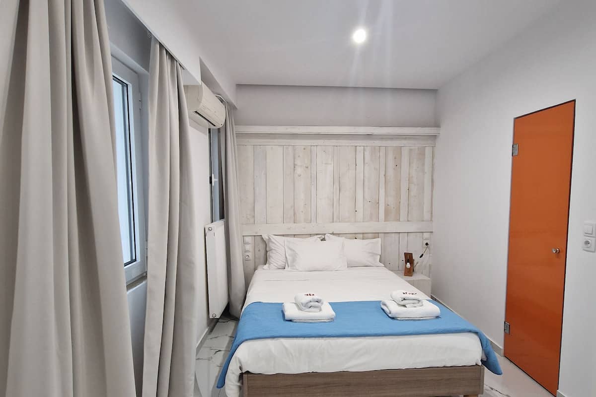 A bedroom with a bed, curtains, a radiator, a door, and a marble floor.