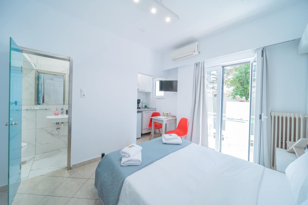 A hotel room with a bed, a desk, a chair, a TV, and a bathroom with a glass shower enclosure.
