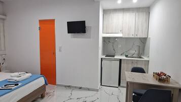 Une chambre d’hôtel compacte comprenant un lit, une petite kitchenette, un coin repas et un téléviseur fixé au mur.