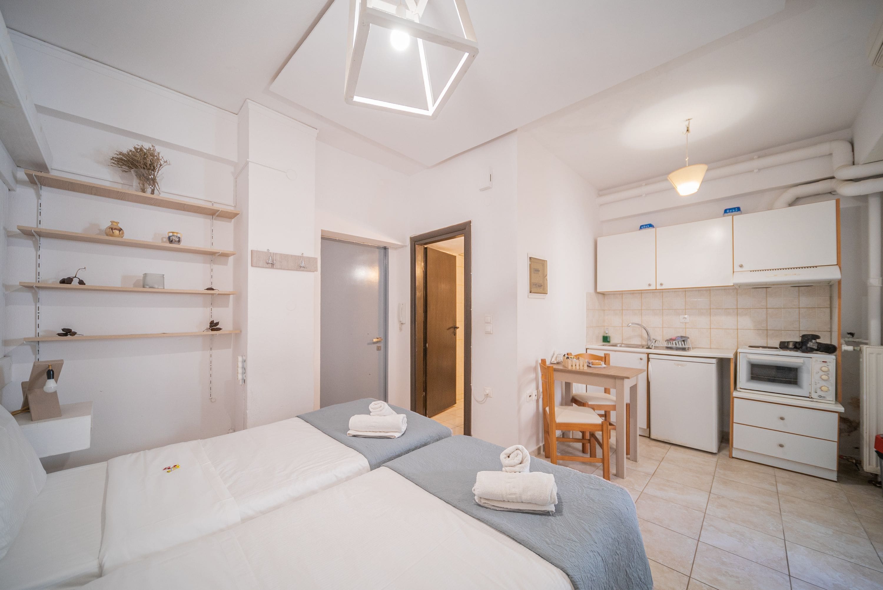 A hotel room with two beds, a small kitchenette, a dining area, and a bathroom.
