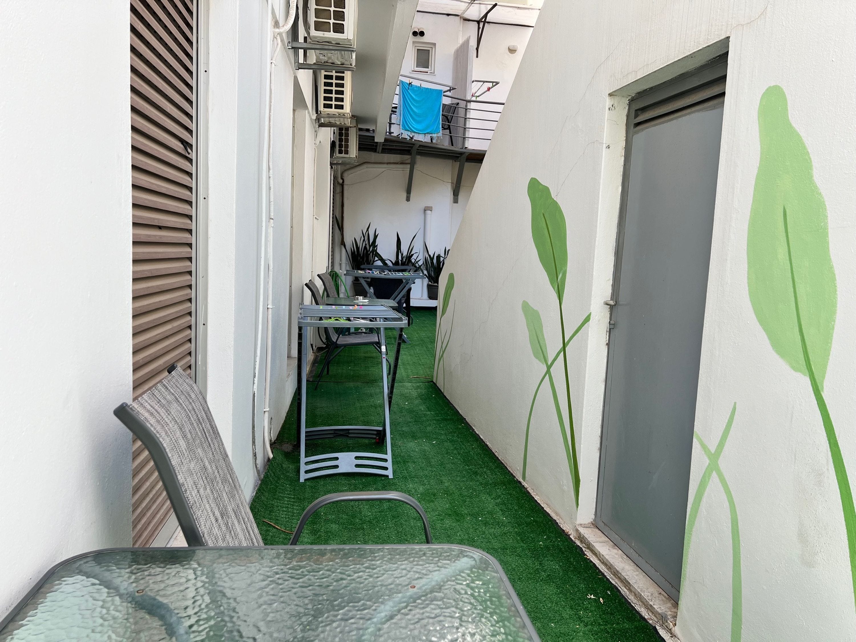 A narrow outdoor space with a table and chairs, a door, and green artificial grass.