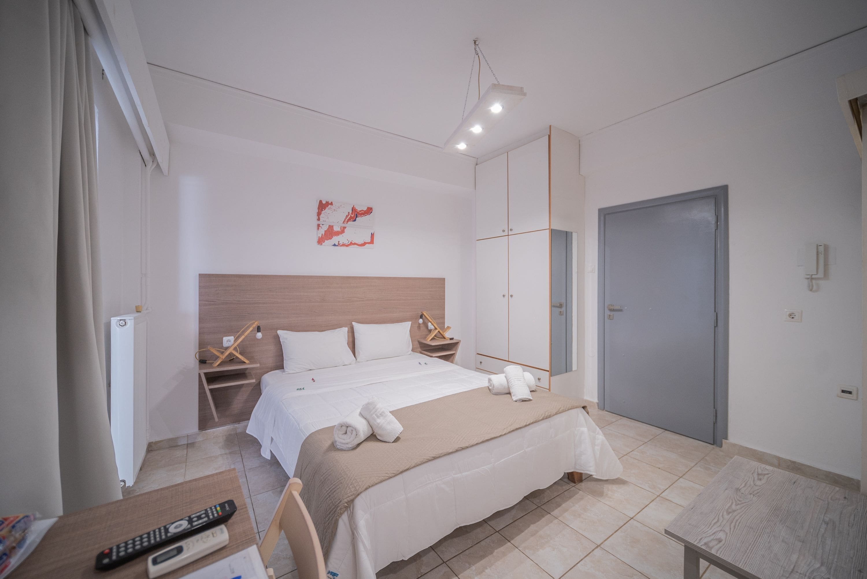 Hotellihuone, jossa on suuri sänky, yöpöytä kaukosäätimellä, vaatekaappi ja ovi.