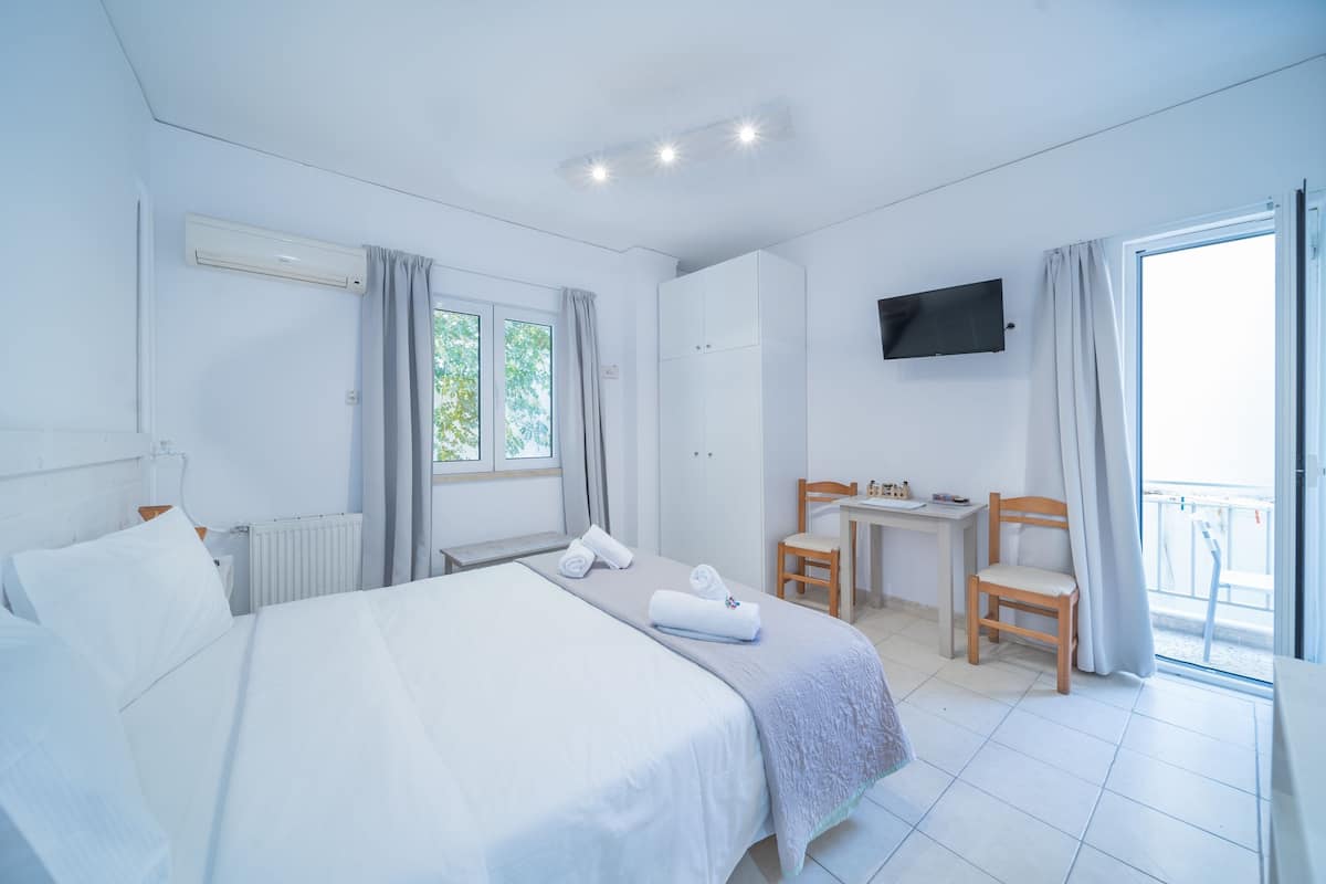 A hotel room with a bed, a desk, a chair, a TV, and a balcony.