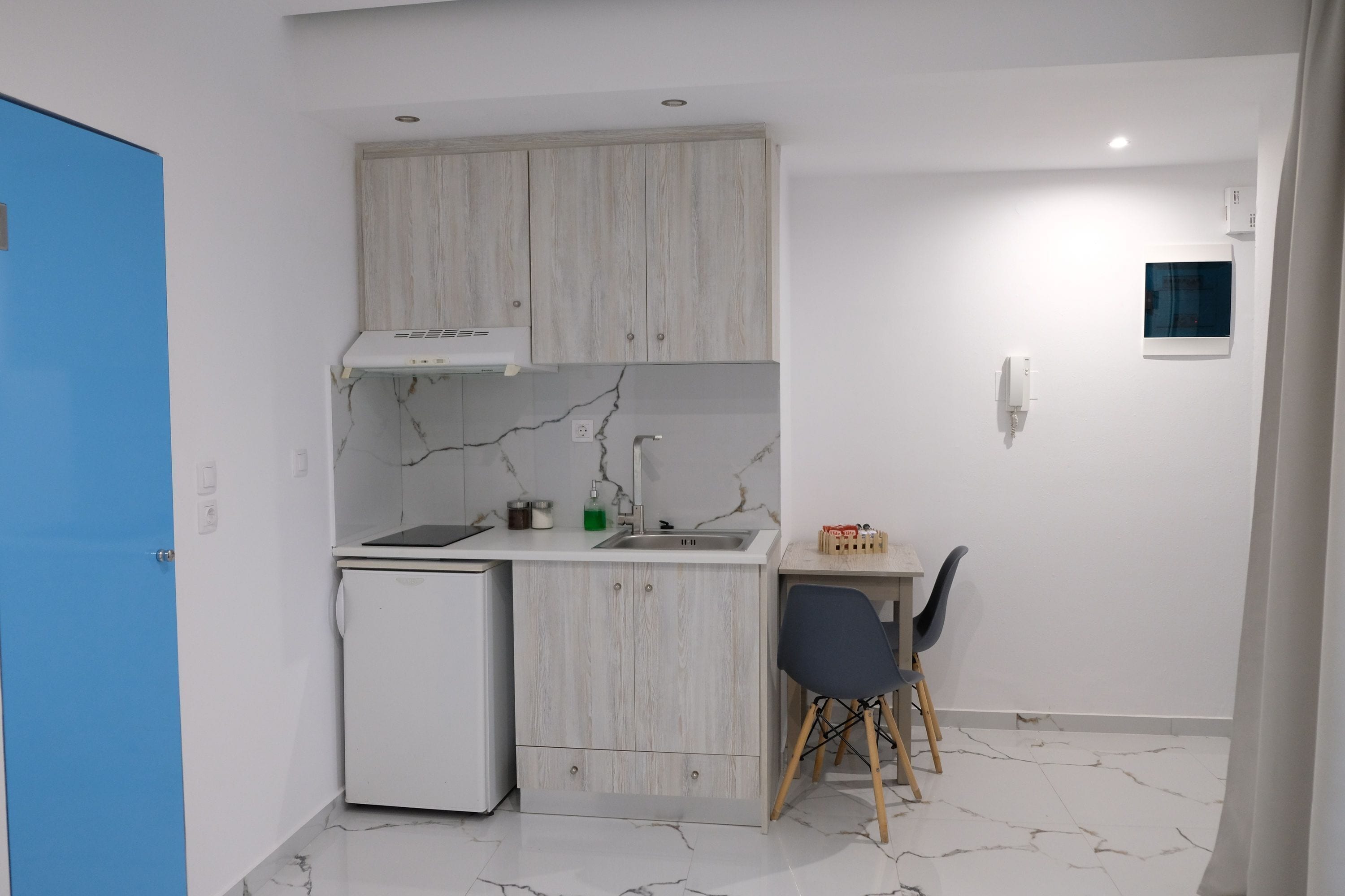 A compact kitchen with a built-in refrigerator, a sink, and a small dining area with a chair.