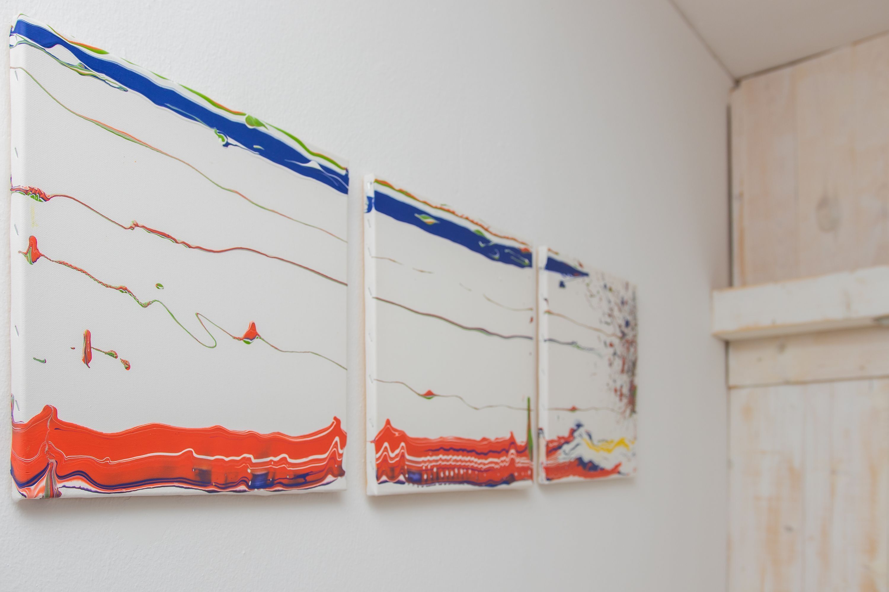 Three abstract paintings on a white wall.