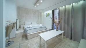 A modern bedroom with a bed, a small table, a chair, and a window with curtains. - City Center Studios by Cretan Houses (Heraklion)