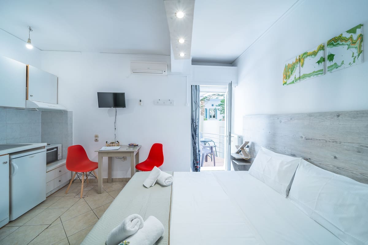 A hotel room with a bed, a desk, a red chair, a television, and a view of the outside.