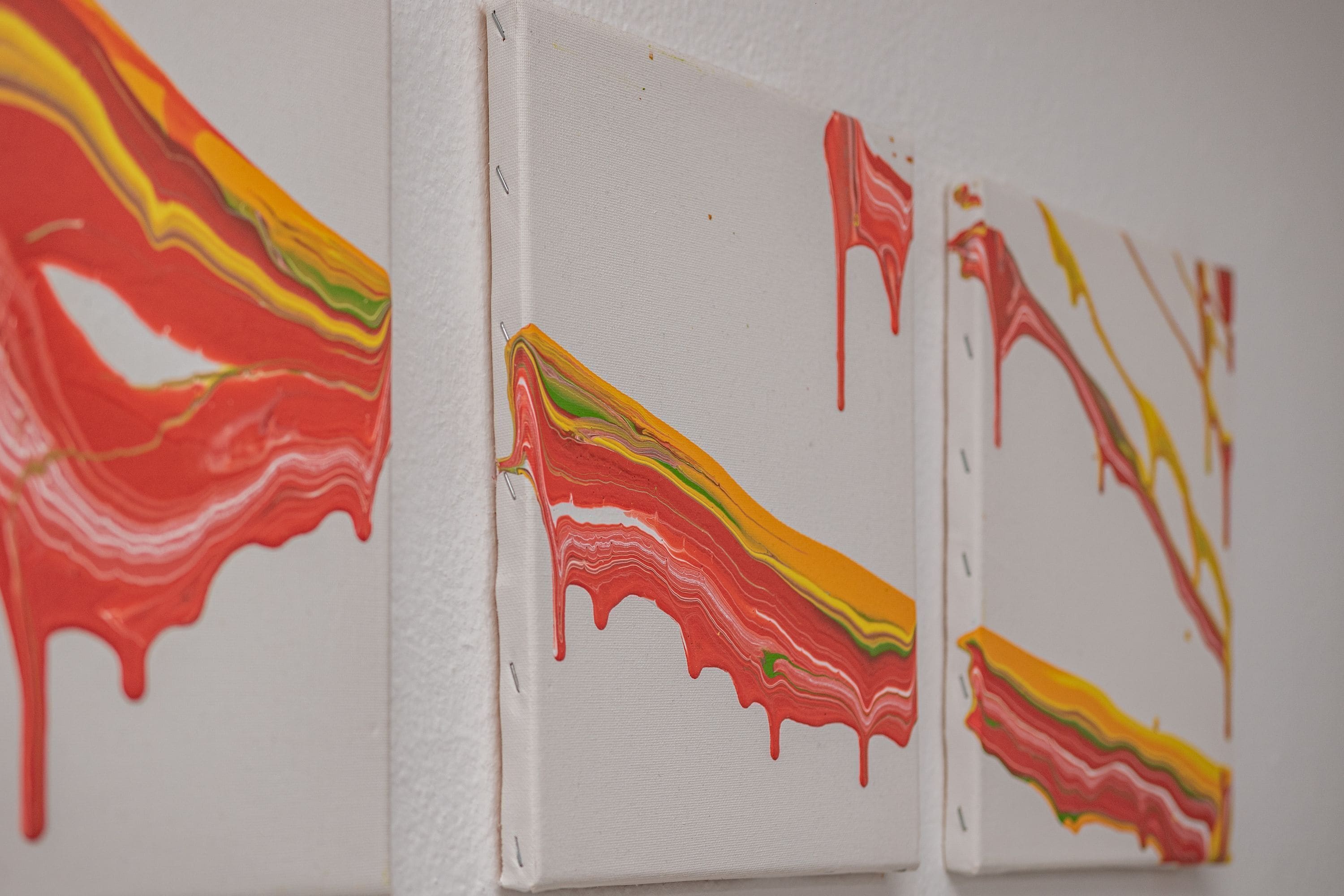 Three white canvases with abstract, colorful drips.