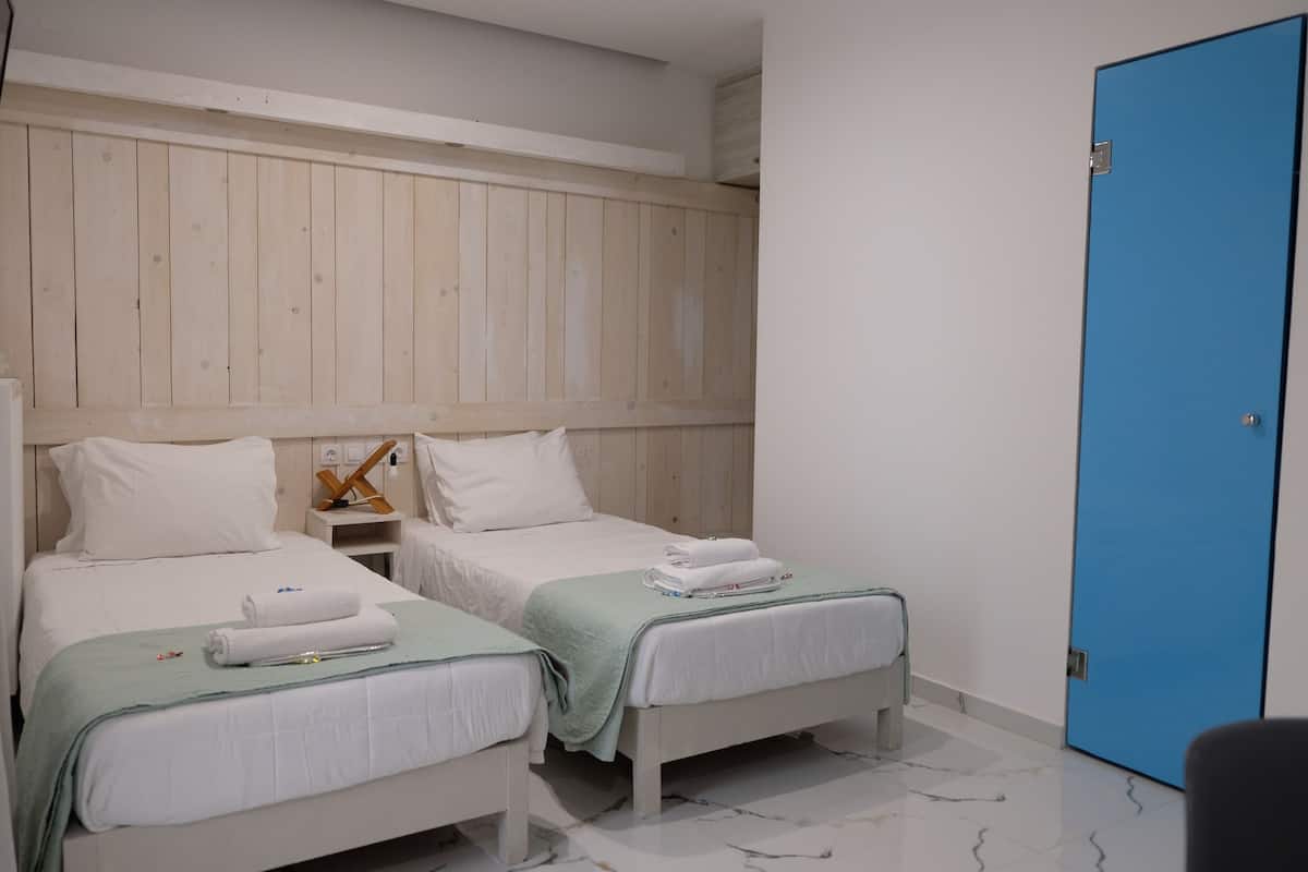 A hotel room with two beds, a wooden headboard, a blue door, and a marble floor.