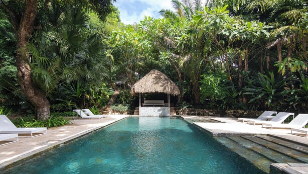 A pool with lounge chairs and a thatched-roof structure surrounded by lush greenery. - Brand New Town House (Puntarenas)