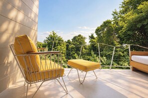 Ein Balkon mit einem gelben Stuhl, einem kleinen Tisch und einem hölzernen Bett.