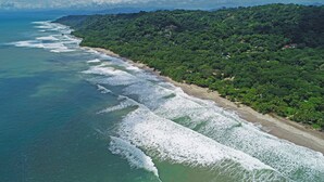 A coastal landscape with a beach, waves, and dense greenery. - Brand New Town House (Puntarenas)