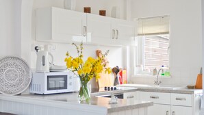 A modern kitchen with white cabinetry, a built-in microwave, a coffee maker, and a vase with yellow flowers. - The Lobster Pot (Seaview)