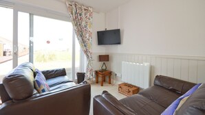 A living room with two sofas, a television, a lamp, and a window with a curtain. - The Lobster Pot (Seaview)