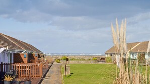 A seaside caravan park with wooden structures, a grassy lawn, and a view of the sea. - The Lobster Pot (Seaview)