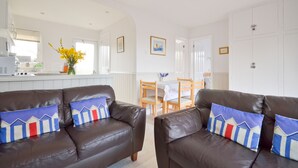 A modern living room with two brown leather sofas, a dining table with chairs, and a kitchen area in the background. - The Lobster Pot (Seaview)