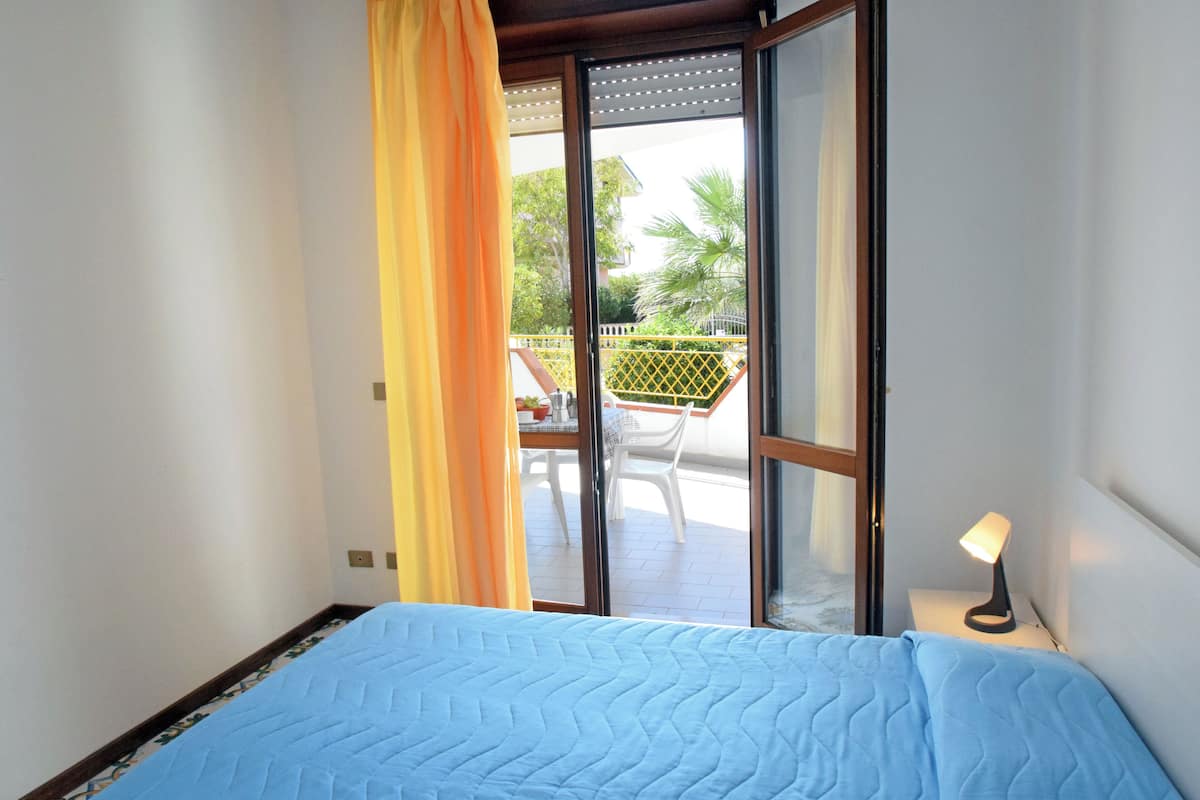 A room with a bed, a sliding glass door leading to an outdoor area with a table and chairs.