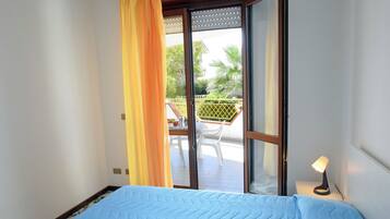 A room with a bed, a sliding glass door leading to an outdoor area with a table and chairs.