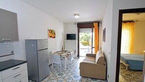 Una cocina compacta con refrigerador, mesa de comedor y sillas. En la habitación contigua hay un sofá y una cama.