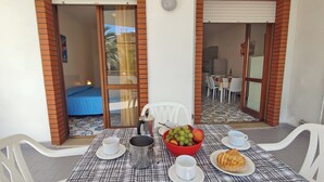 Un comedor con una mesa dispuesta para dos, un frutero, una cafetera y un plato de comida.