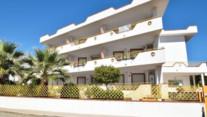 Un edificio de varios pisos con balcones, palmeras y una valla amarilla.
