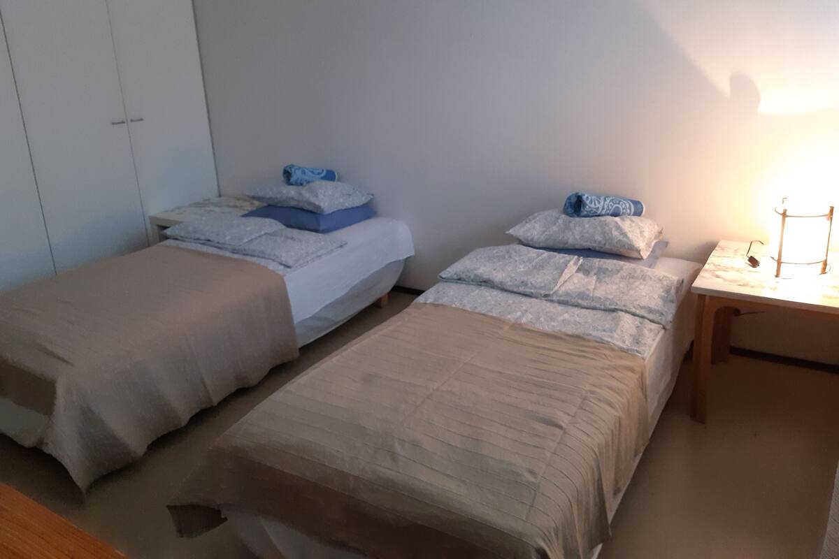 A room with two single beds, a bedside table with a lamp, and a wardrobe.