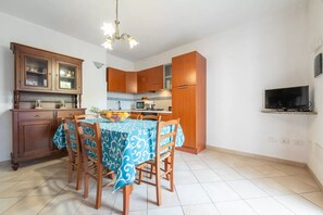 A compact kitchen with wooden cabinets, a dining table with a blue patterned tablecloth, and a television mounted on the wall.