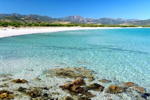 A beach with clear turquoise water, rocky shore, and mountains in the background. - Two Room Flat With Stunning Terrace Near Budoni (Budoni)