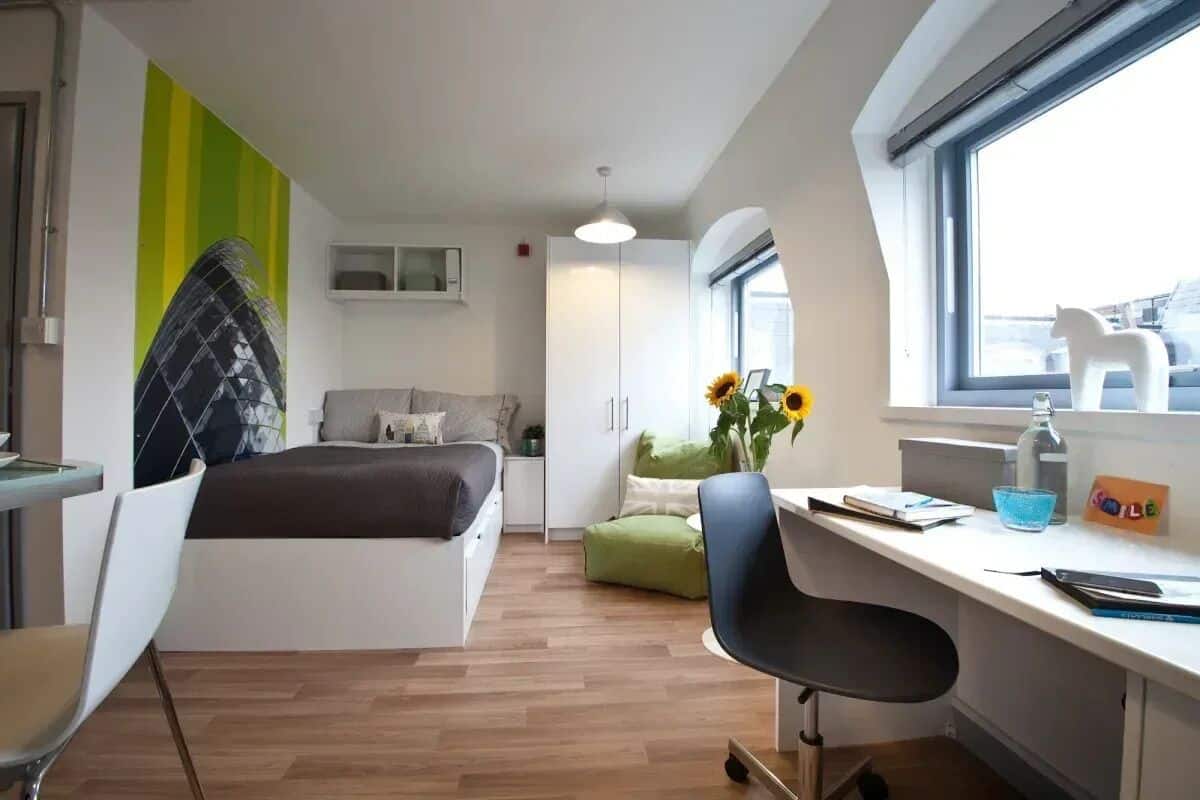 A modern bedroom with a bed, a desk, a chair, a window, and a view of the city.