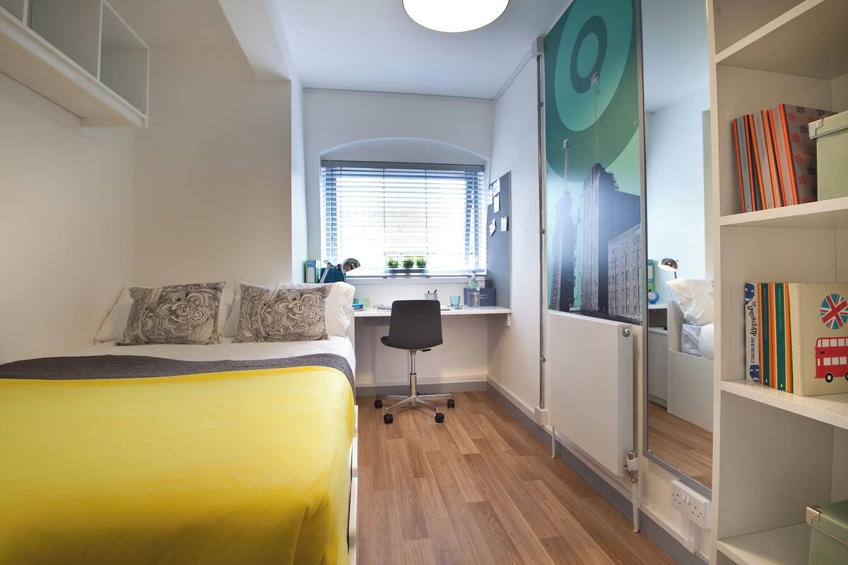 A bedroom with a bed, desk, and bookshelf.