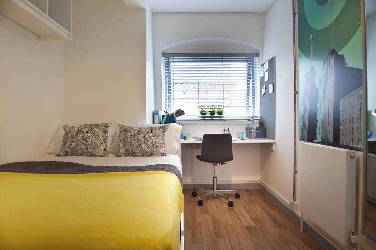 A bedroom with a bed, a desk, and a window.