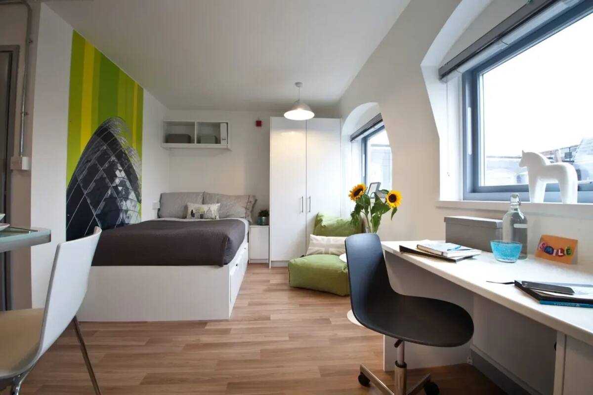 A modern bedroom with a bed, a desk, a chair, and a window.