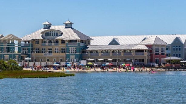 A waterfront hotel with multiple balconies, a pool area, and beach umbrellas. - Sunset Island-Fountain Drive 39-3F-Bayside 67th St, Free WiFi, Pool, Elev, W/D, AC (Ocean City)