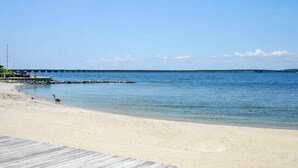 A beach with a wooden boardwalk leading to the water, a pier in the distance, and a clear sky. - Sunset Island-Fountain Drive 39-3F-Bayside 67th St, Free WiFi, Pool, Elev, W/D, AC (Ocean City)