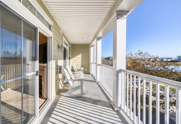 A covered balcony with a view of the beach, white railings, and a door leading to a room.