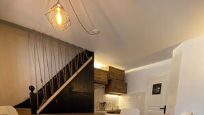 Una cocina moderna con una isla de madera, taburetes blancos y una escalera que sube a un altillo.