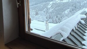Ventana con marco de madera y vista a un paisaje nevado con árboles y montañas.