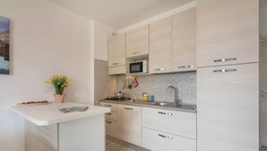 Una cocina moderna con armarios blancos, microondas, pileta y una pequeña isla con una planta.