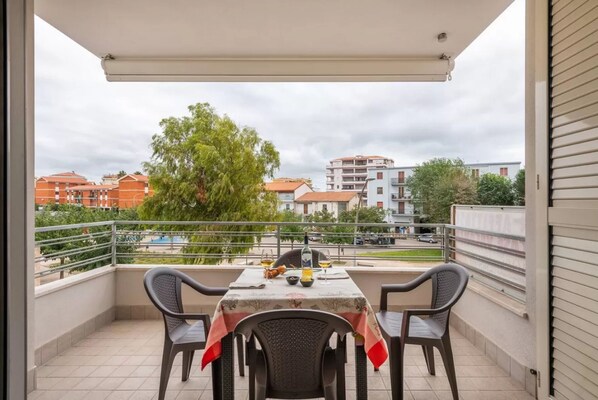 Un balcon avec une table dressée pour deux personnes, des chaises et une vue sur les bâtiments et les arbres.