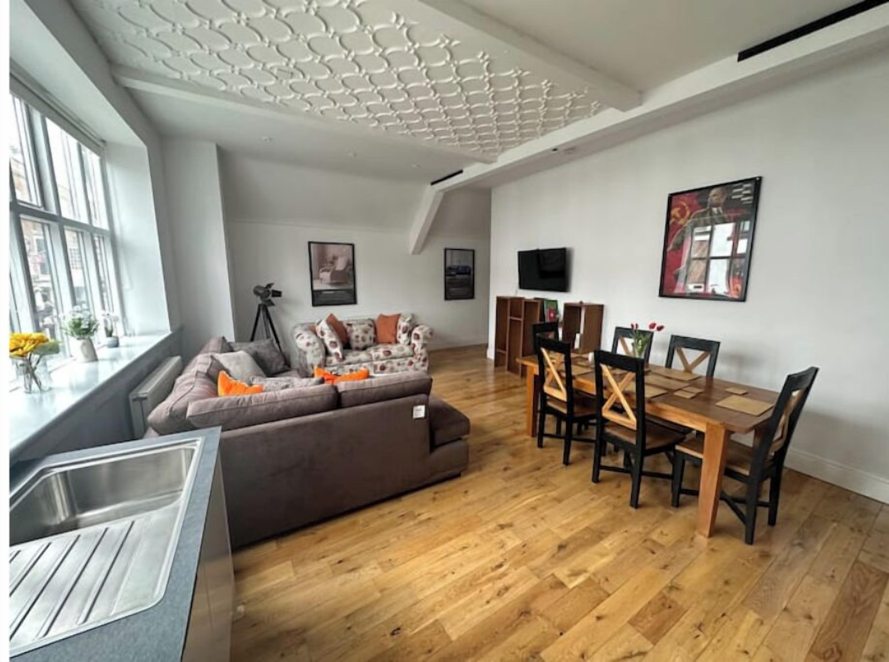 Un salon moderne avec un canapé, une table à manger et des chaises. On aperçoit un trépied et un téléviseur fixés au mur.
